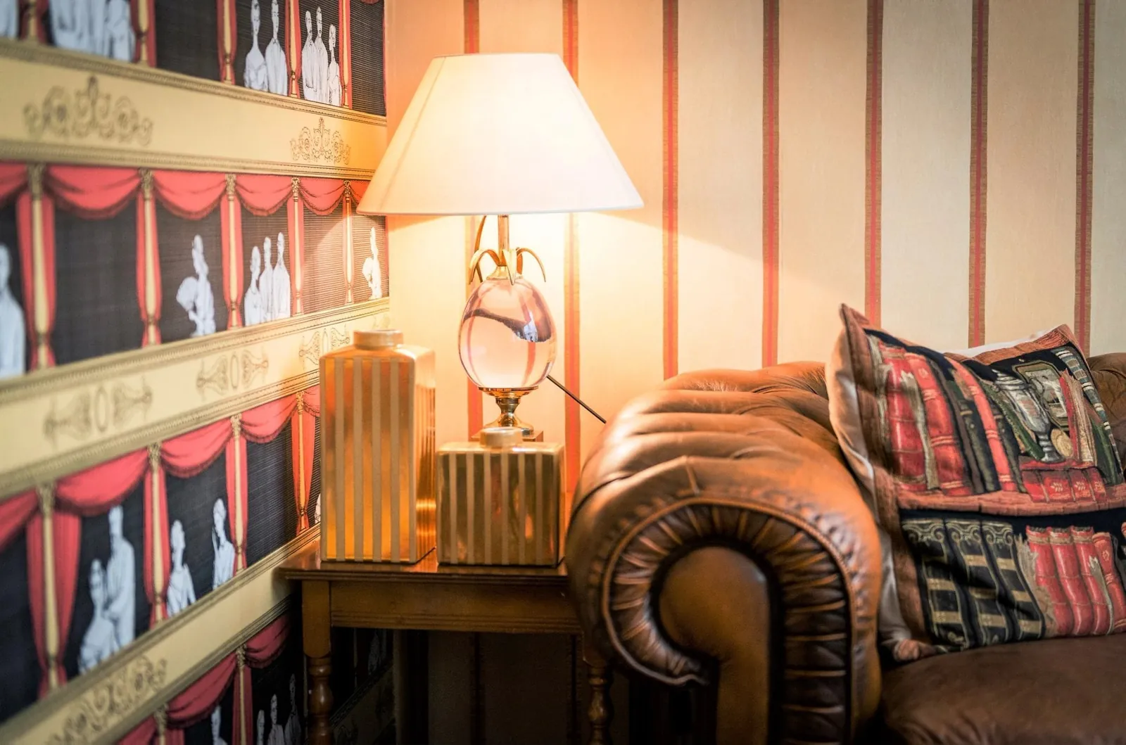 Salon bibliothèque de l'Hôtel du Théâtre, papier peint rayé façon théâtre, canapé en cuir et lampe