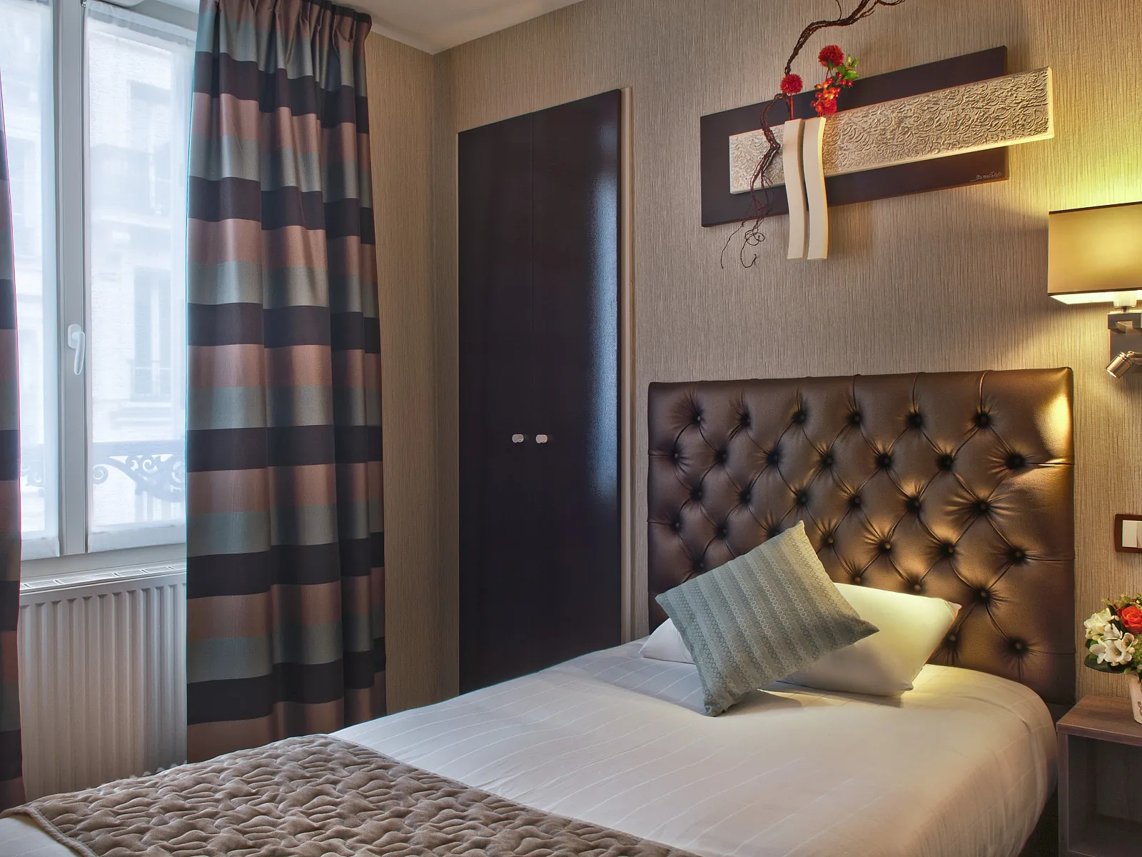 Single room at Hôtel France Albion with a tufted brown leather headboard, striped curtains and warm lighting