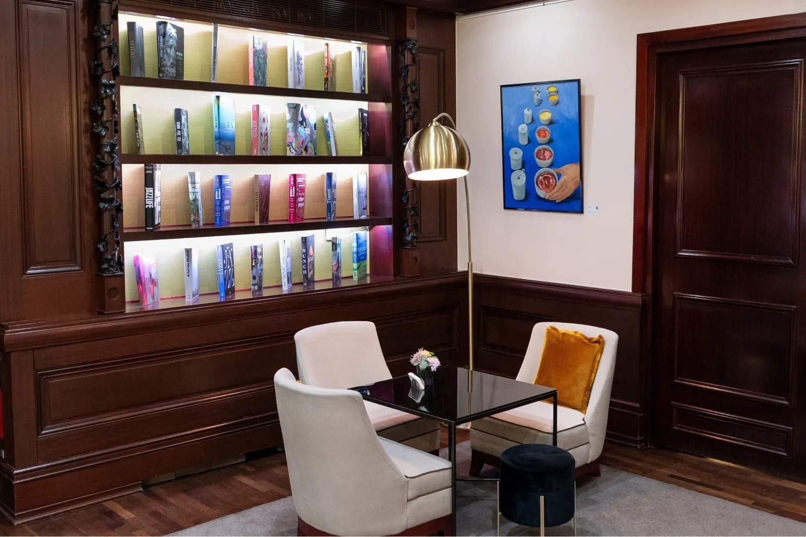 Salon bibliothèque de l'Hôtel Pont-Royal à Paris, étagères éclairées, fauteuils crème et boiseries
