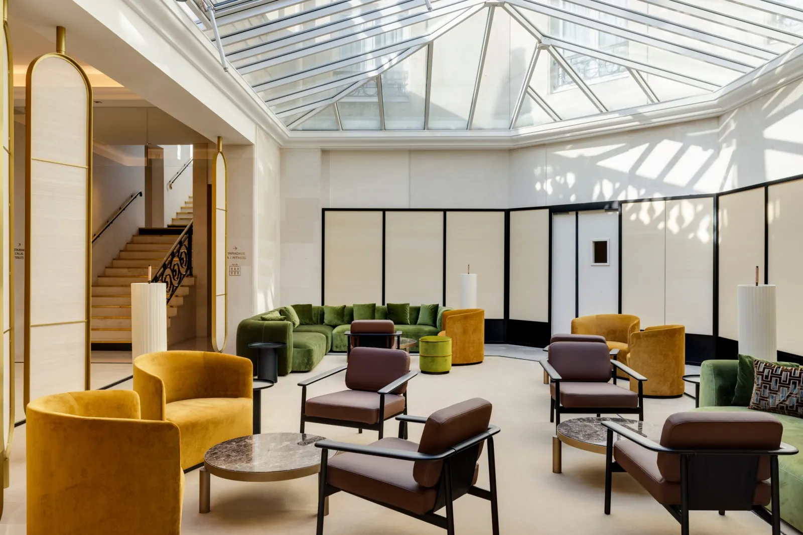 Glass-roofed lounge with gold armchairs and green sofas at InterContinental Chantilly Château Mont Royal