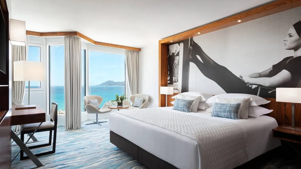 Deluxe room with sea-view balcony doors, white bed and black-and-white mural at JW Marriott Cannes