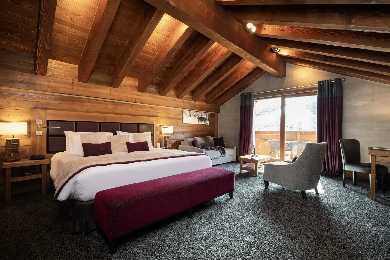Chambre aux poutres apparentes, banc bordeaux et vue depuis le balcon au Kaïla, Méribel
