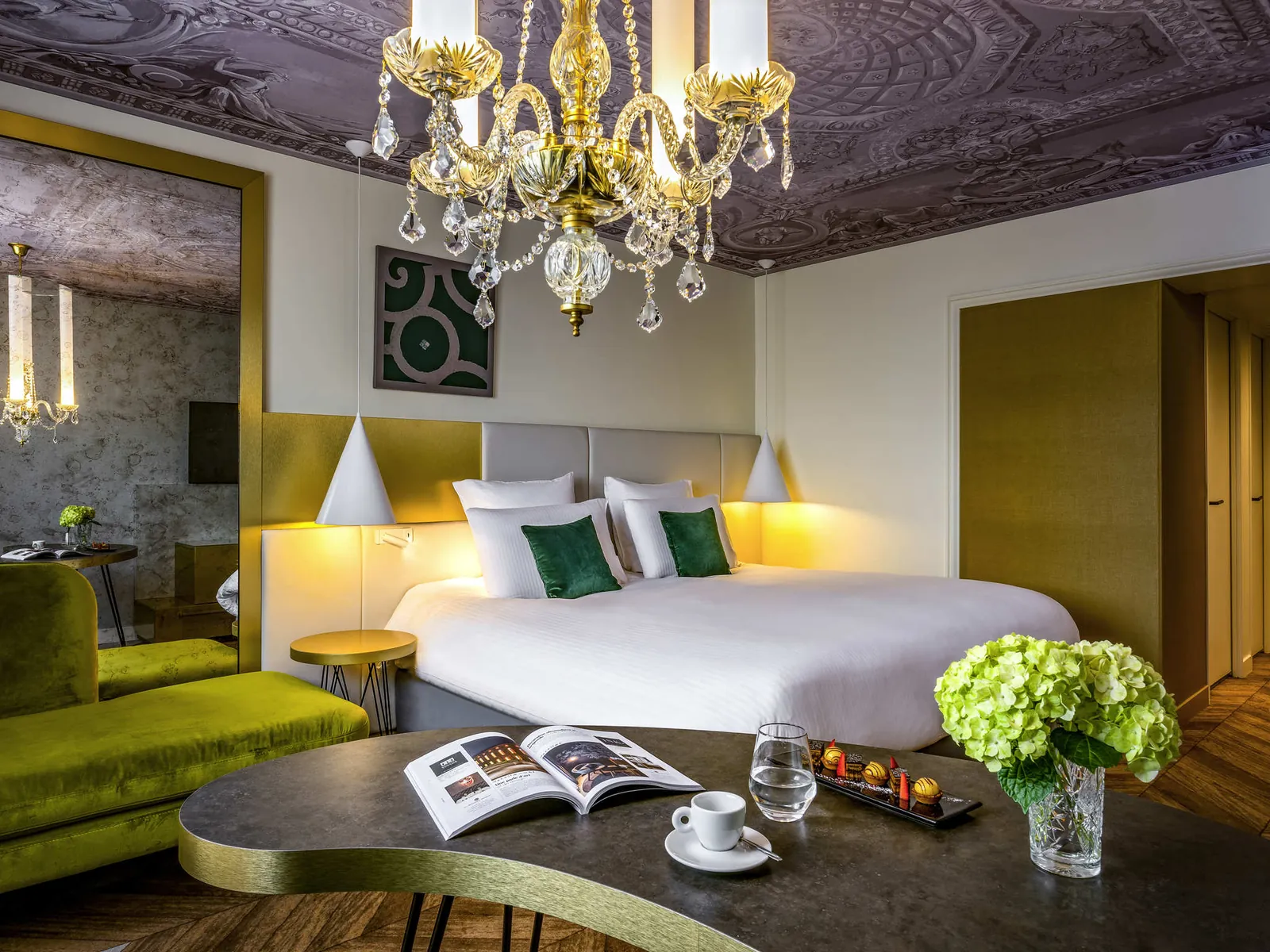 Bedroom with a green sofa, gilded chandelier and patterned ceiling at Le Louis Versailles, Versailles