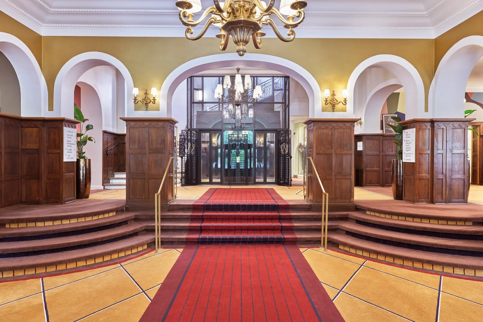 Grand entrance hall with a red carpet, carved wood and a chandelier at Hôtel Barrière Le Westminster
