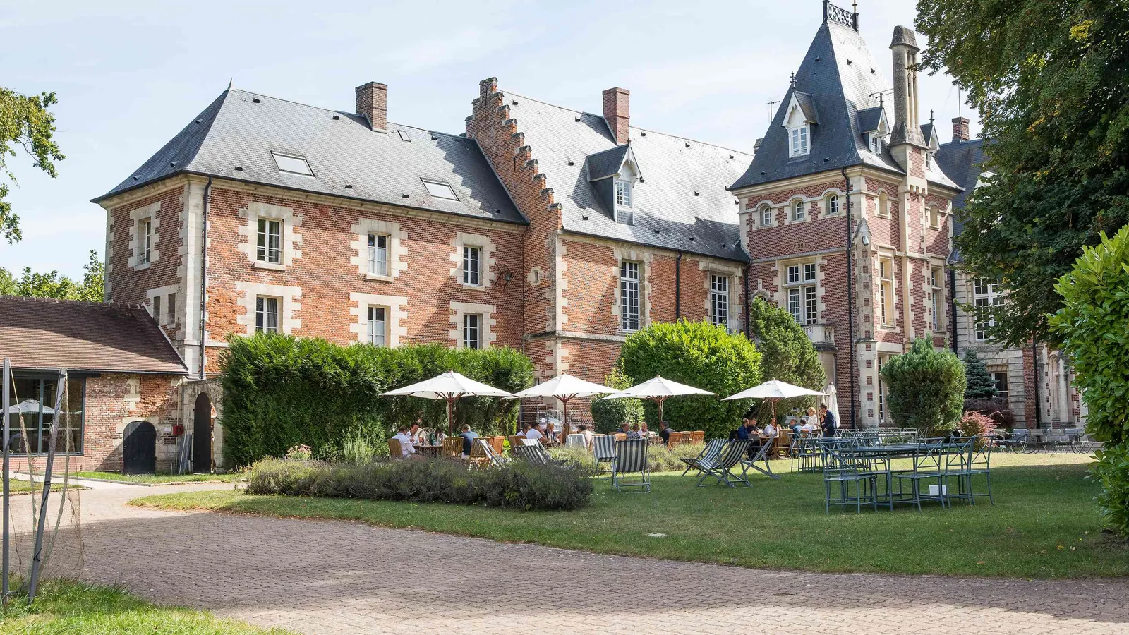 Manoir en brique rouge avec parasols sur la terrasse et pelouse au Manoir des Plaines Picardes, Oise