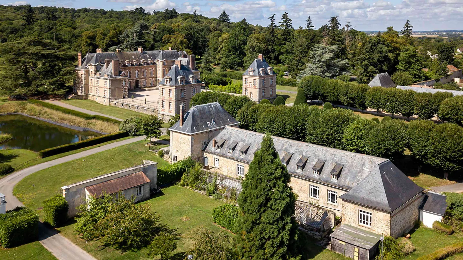 Manoir et dépendances au bord d'un étang et de haies taillées au Manoir des Prés Fleuris, Yvelines