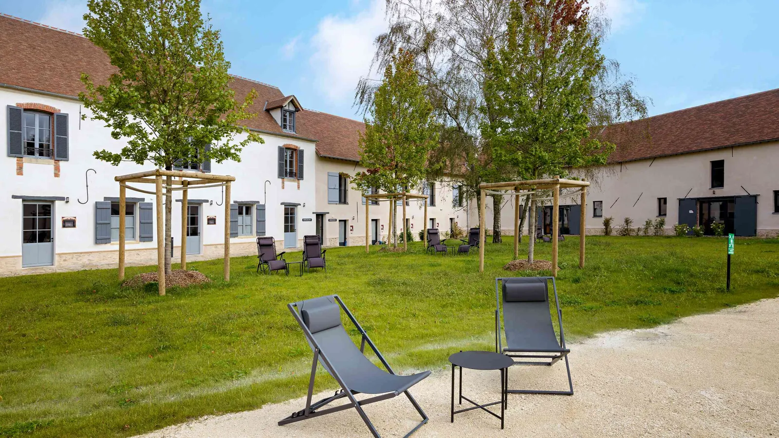 Courtyard of Manoir des Saules Dorés lined with converted outbuildings, deckchairs and young trees