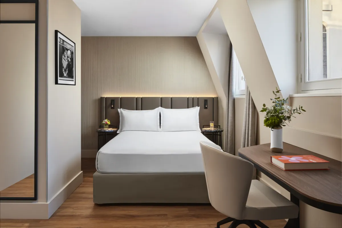 Chambre standard du NH Paris Gare de l'Est avec lit fait, bureau en bois et fauteuil gris sous les combles