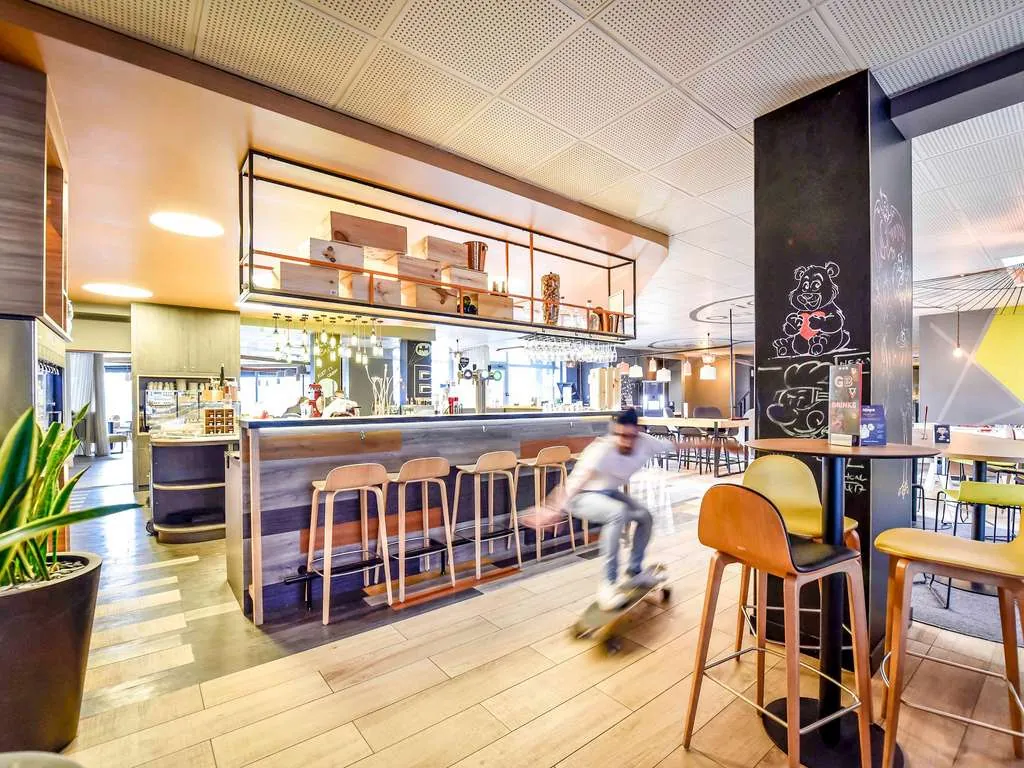 Bar area with high stools and wood counter, lit by pendant lights at Novotel Bordeaux Lac, Bordeaux
