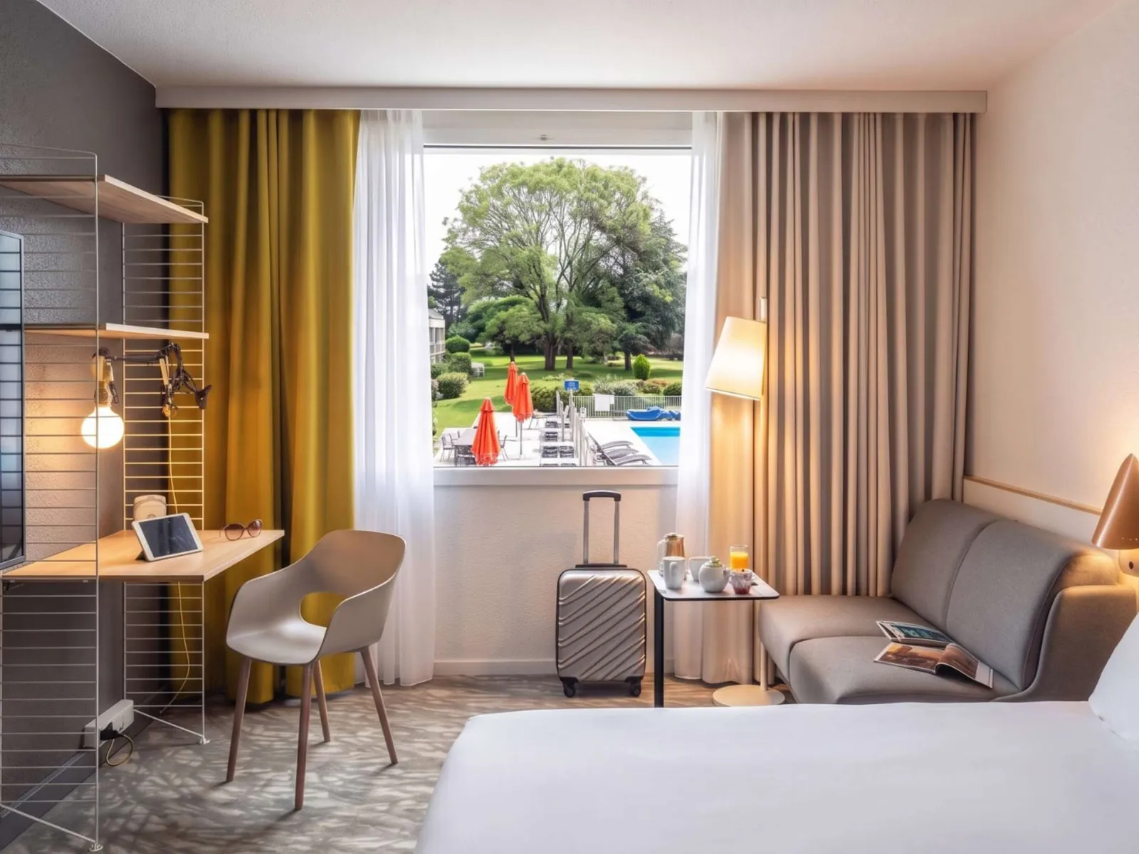 Guest room with a view of the garden and a grey sofa at Novotel Évry-Courcouronnes, Évry