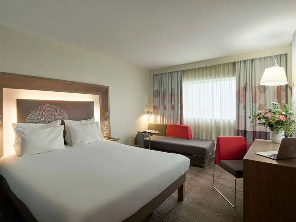 Double guest room with a white bed, red armchair and desk at Novotel Paris La Défense Esplanade