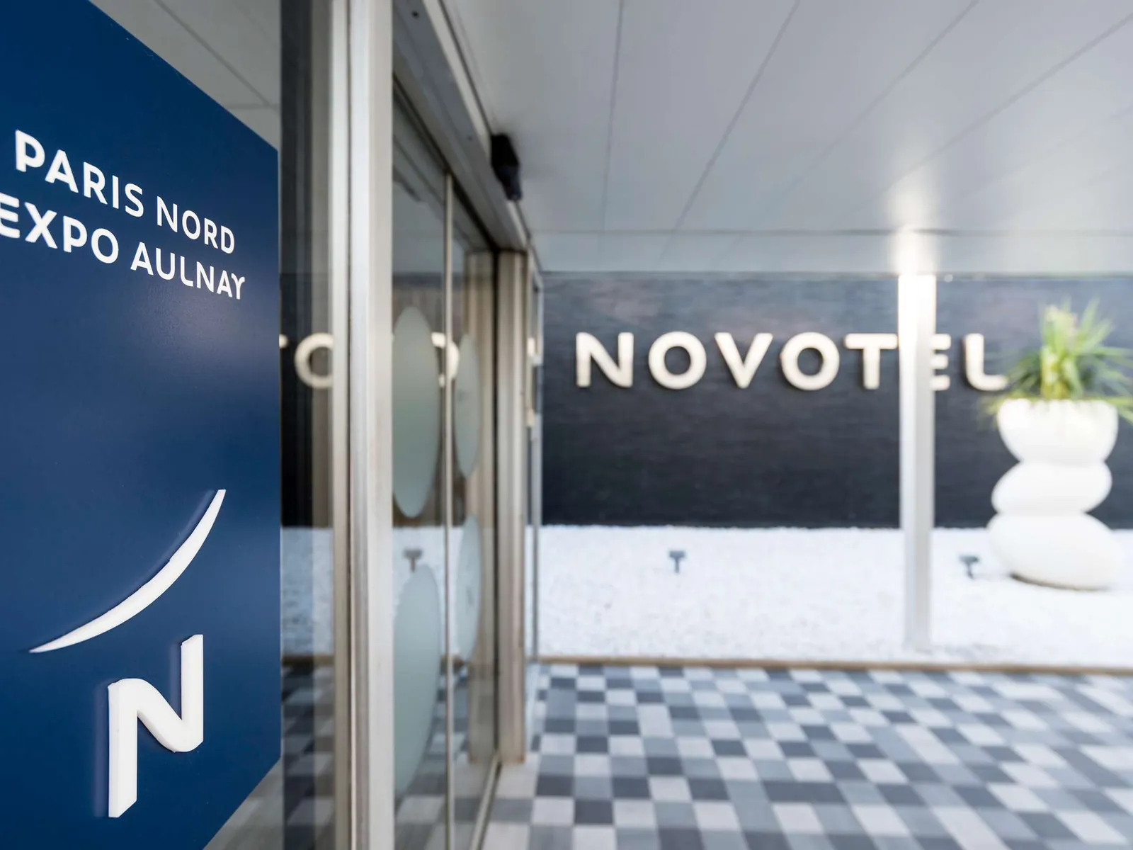 Glass entrance hall with the Novotel sign and checkered floor at Novotel Paris Nord Expo Aulnay