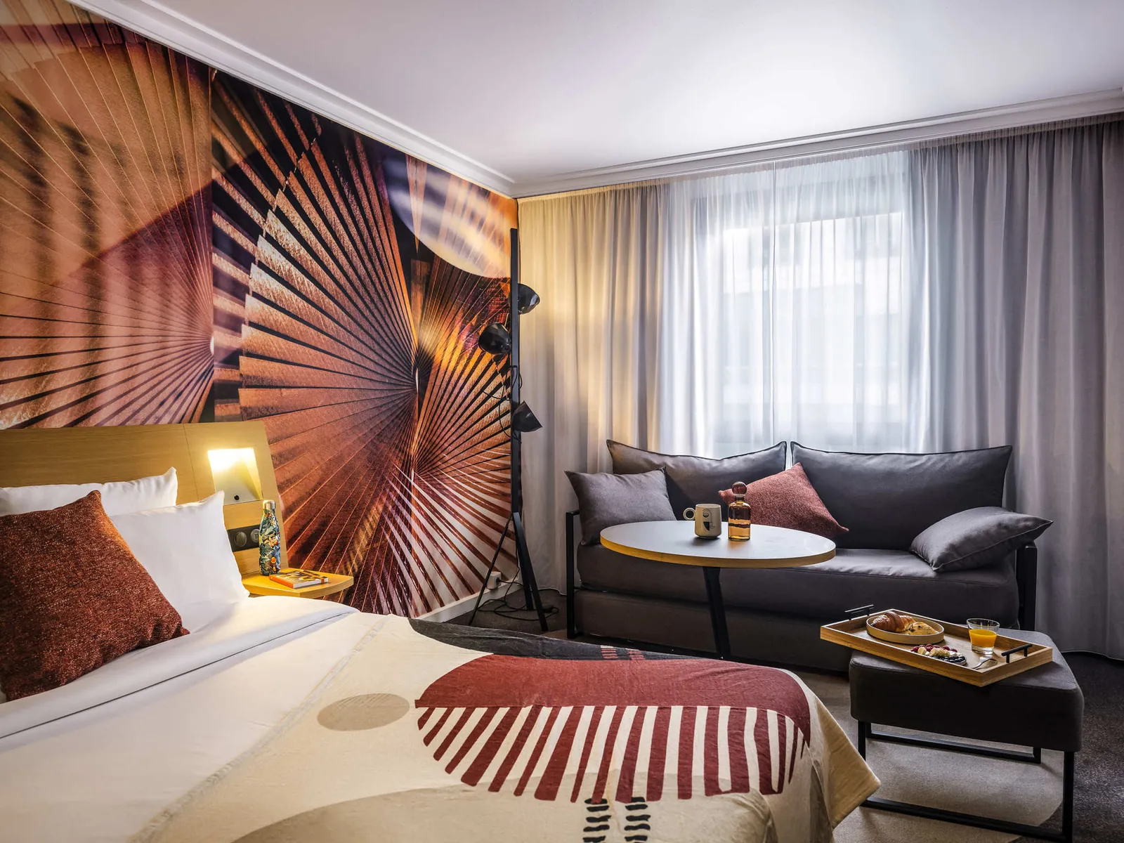 Room with sunburst wall art, a grey sofa and a bed at Novotel Paris Vaugirard Montparnasse, Paris
