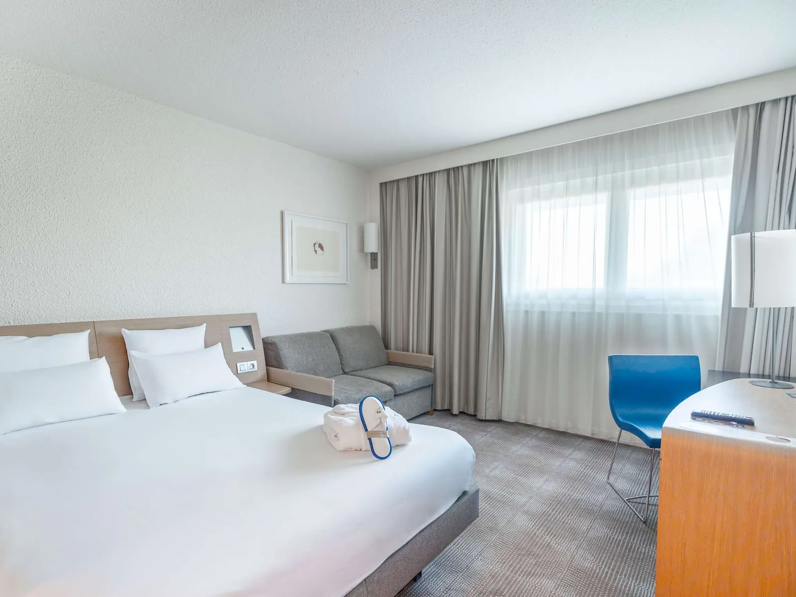 Double room with a sofa bed, desk and blue armchair at Novotel Poissy Orgeval, Yvelines