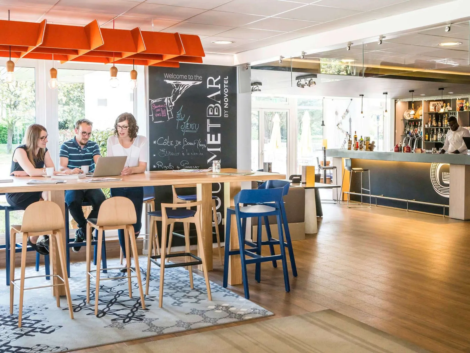 Bar lounge with an orange ceiling, high stools and a chalkboard menu at Novotel Saclay, Essonne