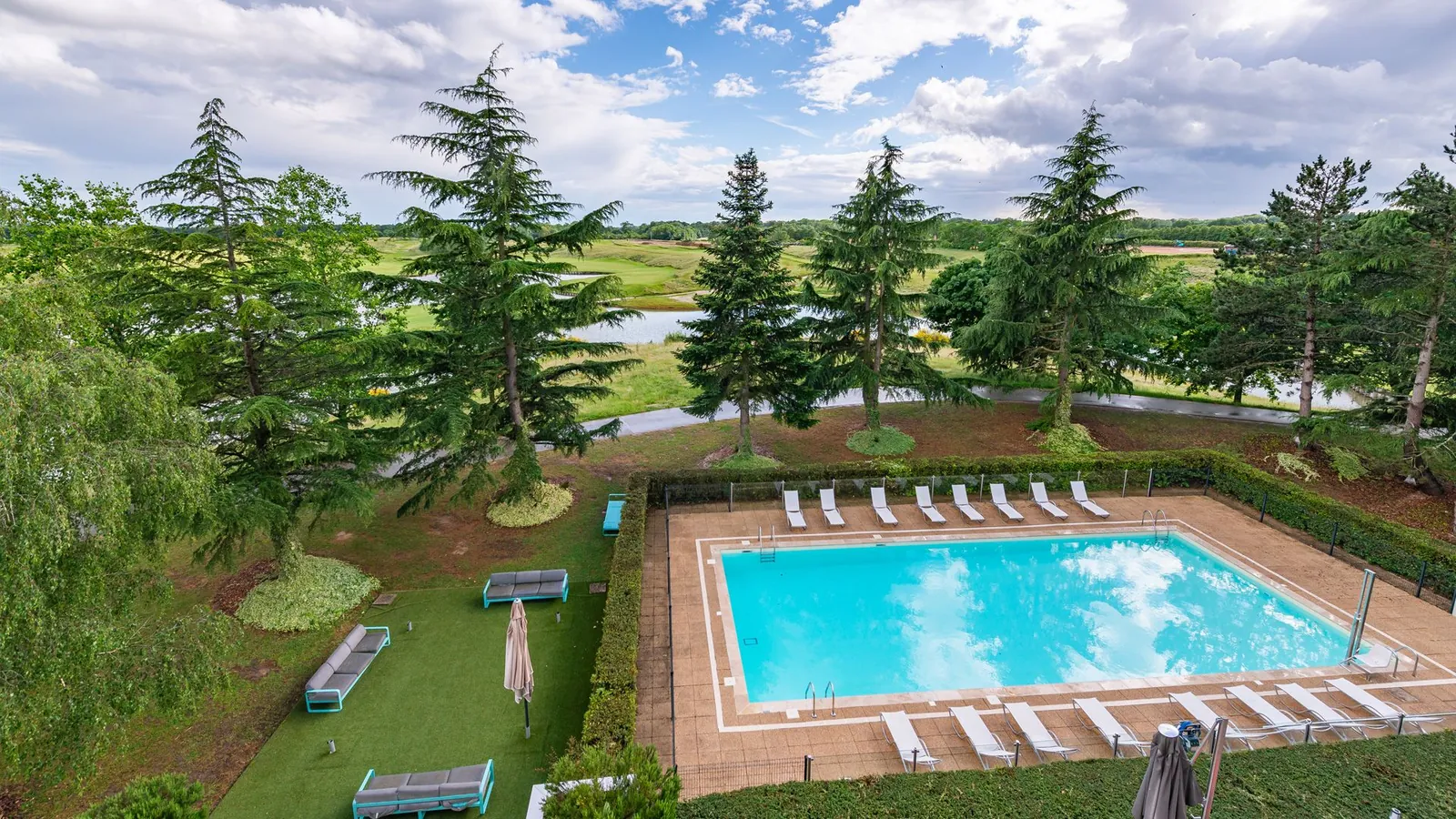 Outdoor pool surrounded by pine trees and lawns at Novotel Saint-Quentin-en-Yvelines Golf National