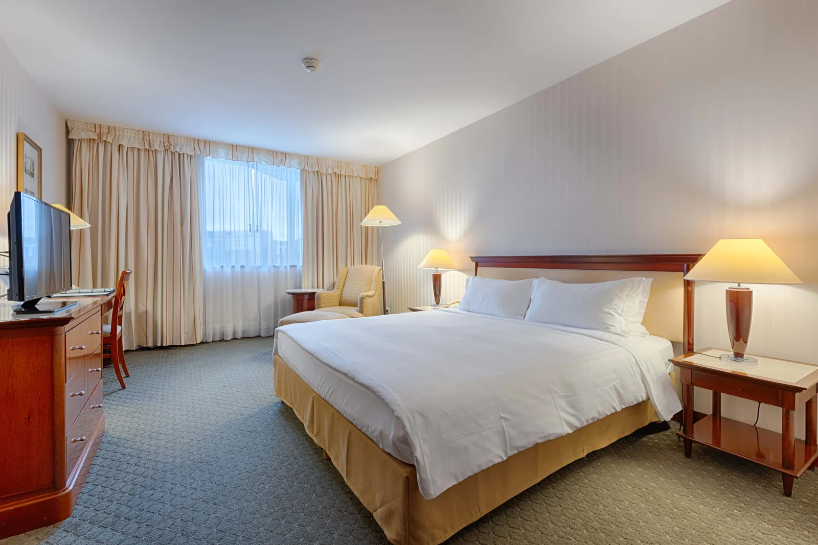 Superior room with a king bed, wooden furniture and a tall window at Occidental Paris Levallois