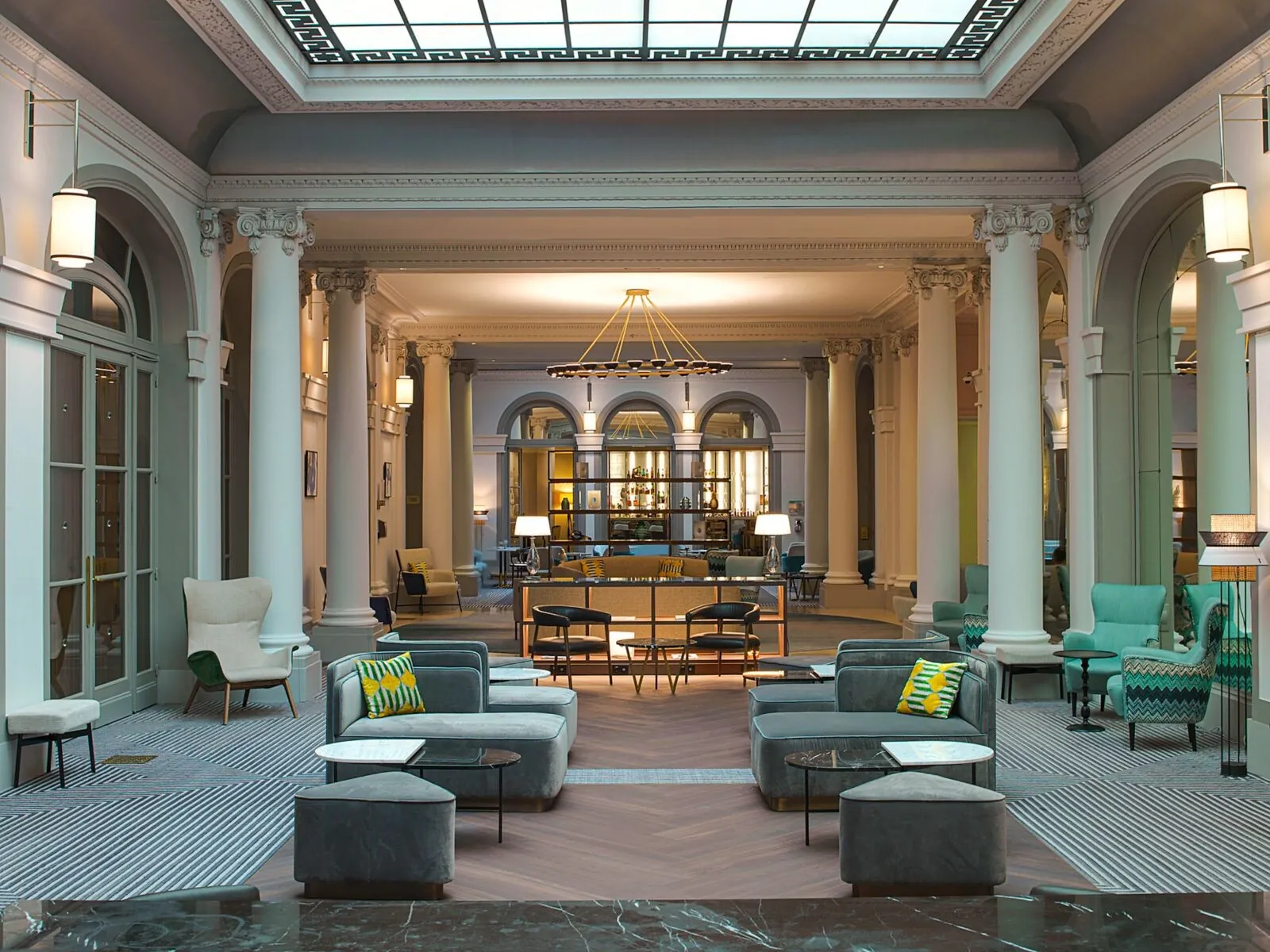 Lounge area of the Paris Marriott Opera Ambassador Hotel with columns, turquoise armchairs and a glass ceiling