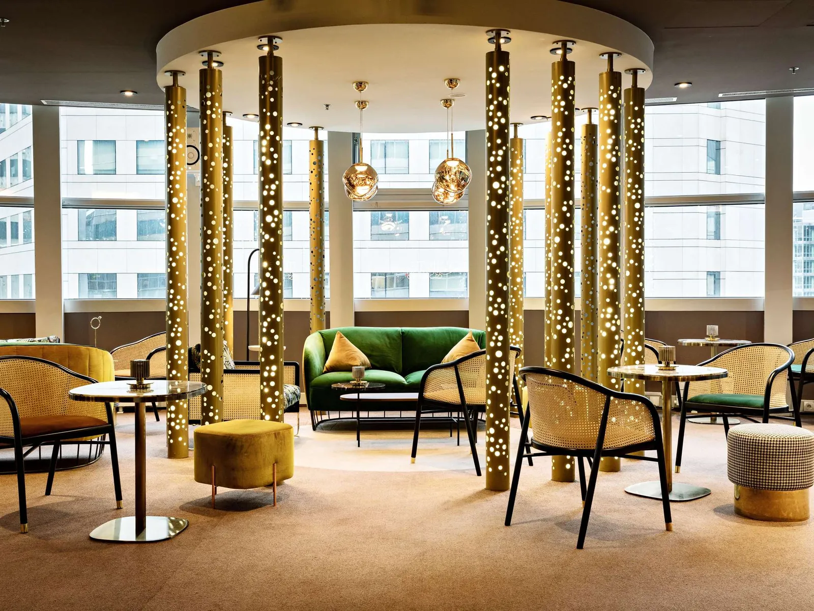 Lounge bar with gold-clad columns, a green sofa and lounge chairs at Pullman Paris La Défense