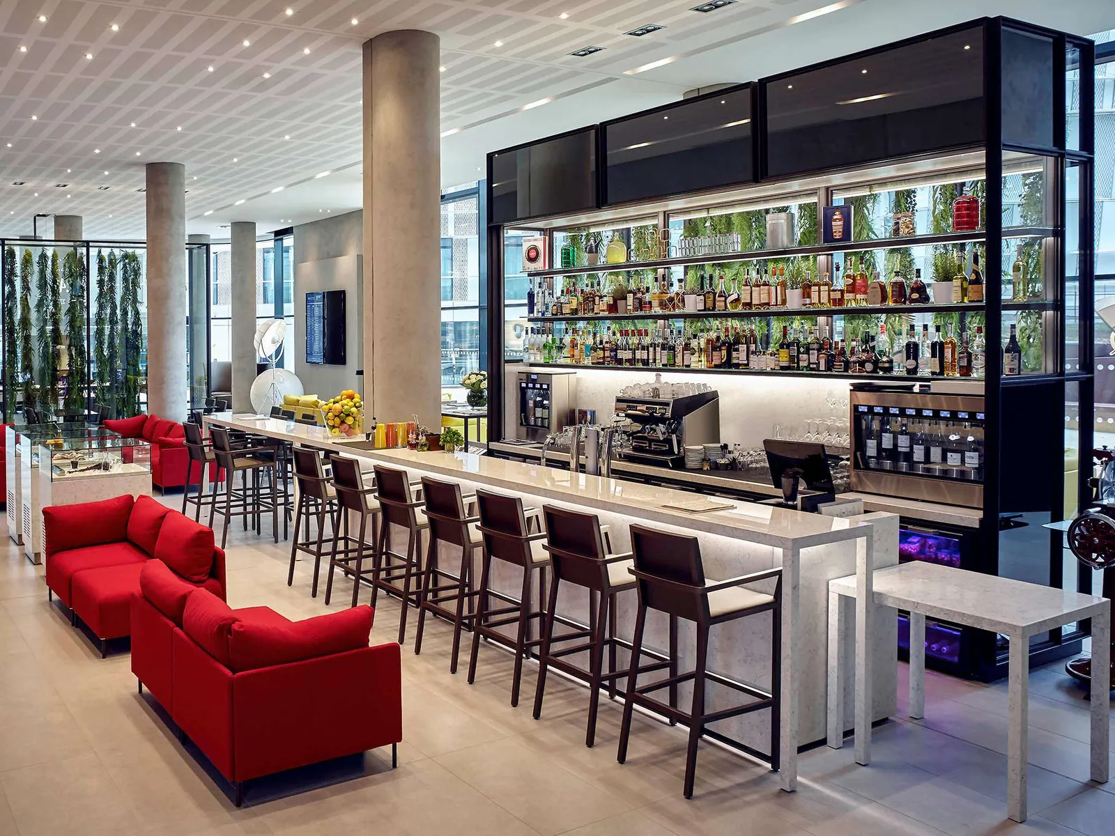 Bar et lounge du Pullman Paris Roissy CDG Airport avec canapés rouges, tabourets et bouteilles