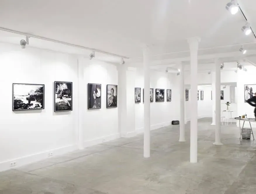 White gallery room with framed black-and-white prints on the walls and white columns