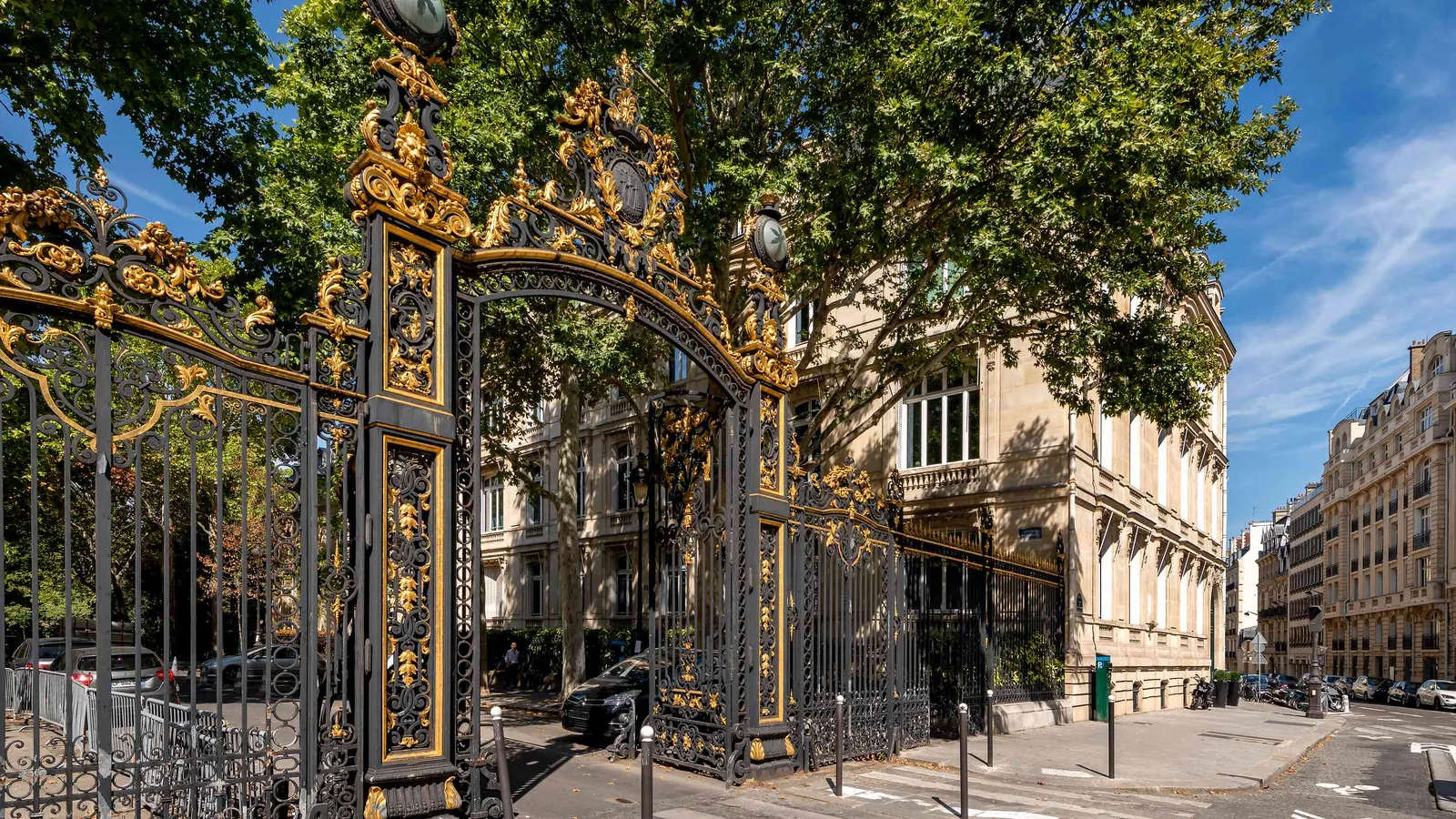 Extérieur de l'Atelier Lumière avec grille dorée ouvragée et rue parisienne bordée d'arbres