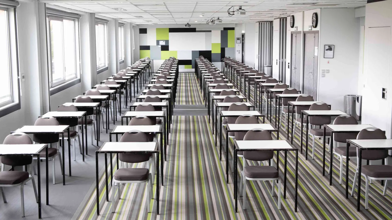 Salle de séminaire des Ateliers du Nord en rangées de tables, murs colorés et moquette rayée