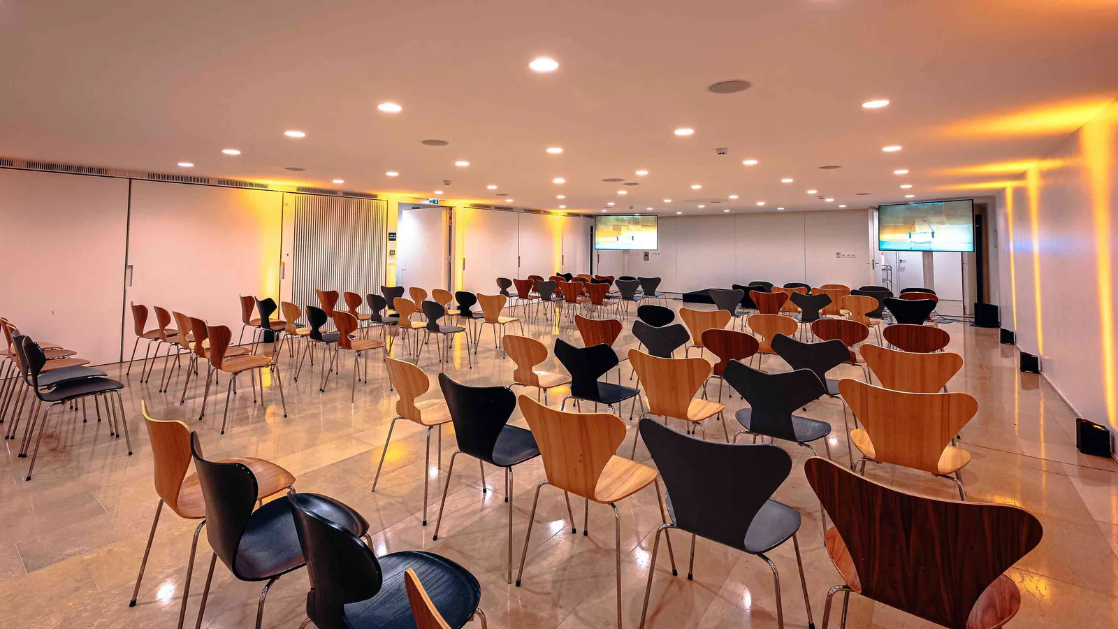 Left Bank Atrium seminar room set in rows of chairs with ceiling spots and wall screens