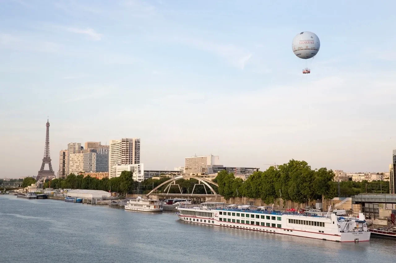 Vue sur la Seine avec le ballon captif, la tour Eiffel au loin et une péniche de croisière amarrée.