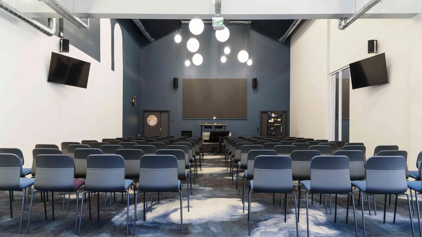 Grande salle du Belvédère Nord avec sièges en rangées, écrans muraux et suspensions