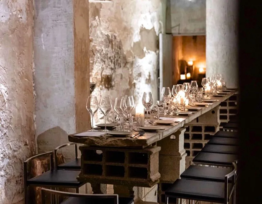 Loft with raw concrete walls, a long dining table and a dark bar