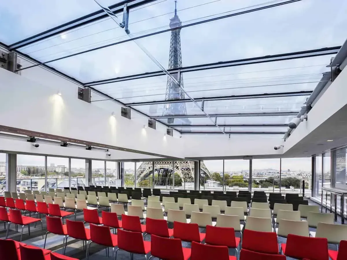 Glass hall with rows of red seating and the Eiffel Tower visible through the roof