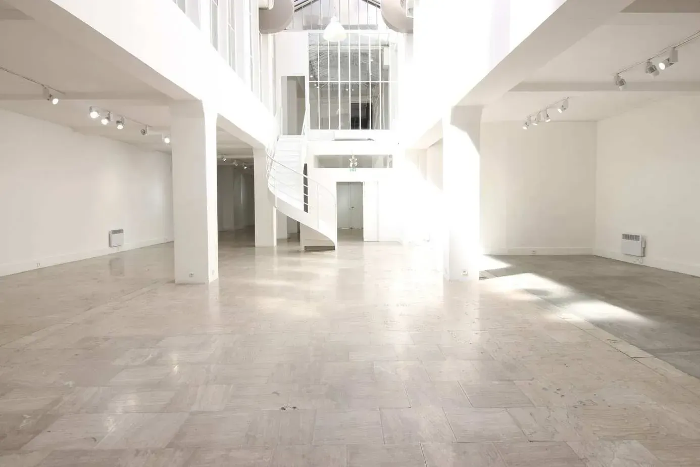Hall blanc avec escalier courbe, colonnes hautes et plafond vitré