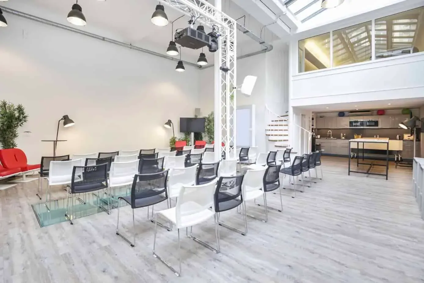 Bright room under a glass roof set with rows of chairs facing a presentation area