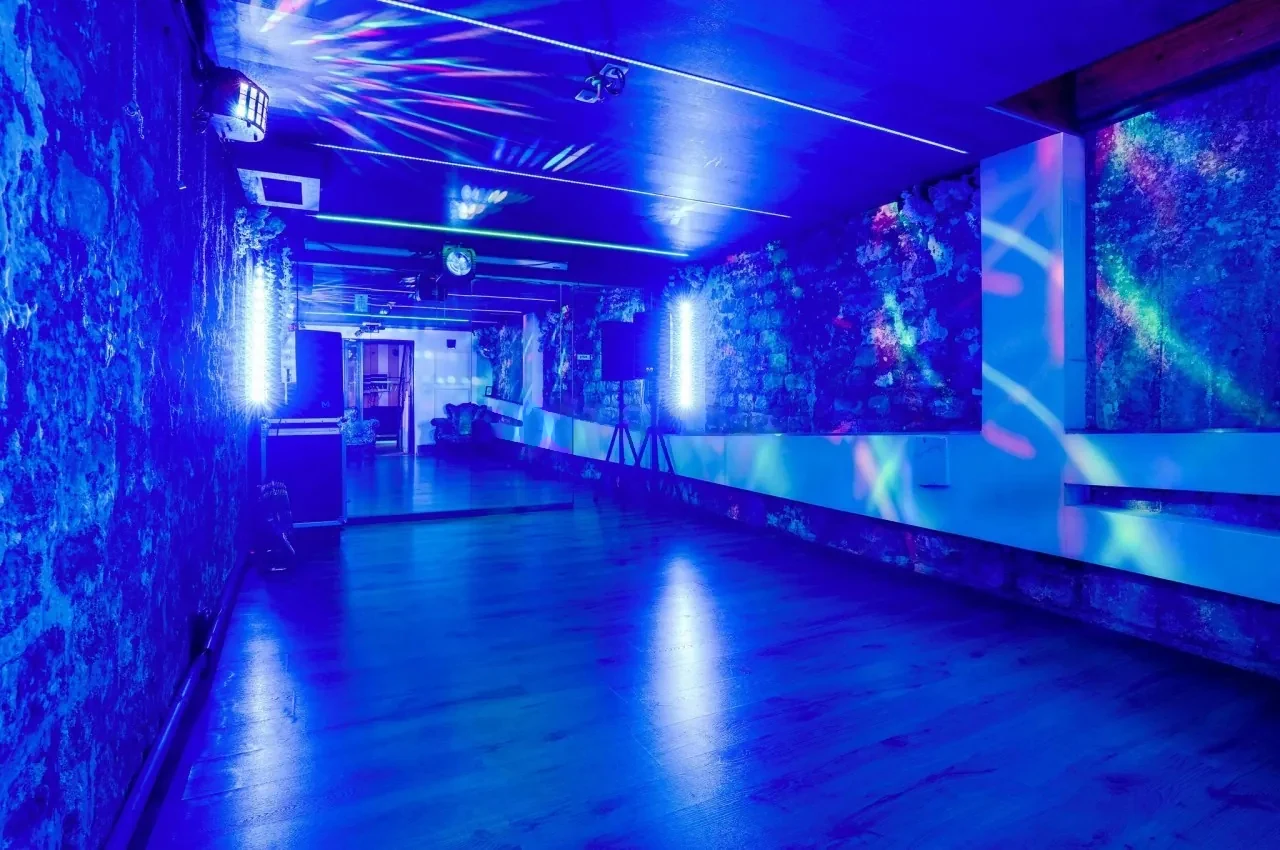 Dance room lit in blue with a sound and light rig and textured stone walls.