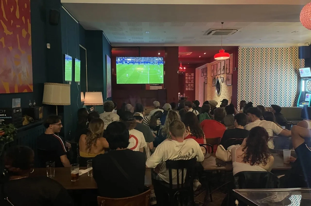 Lounge area with a screen showing a match and seated guests
