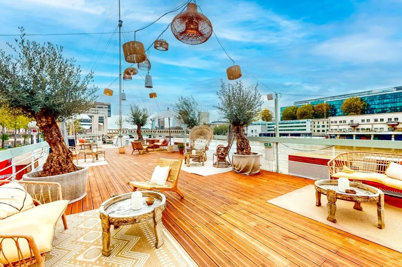 Sun deck with wooden flooring, rattan furniture and olive trees on the Seine