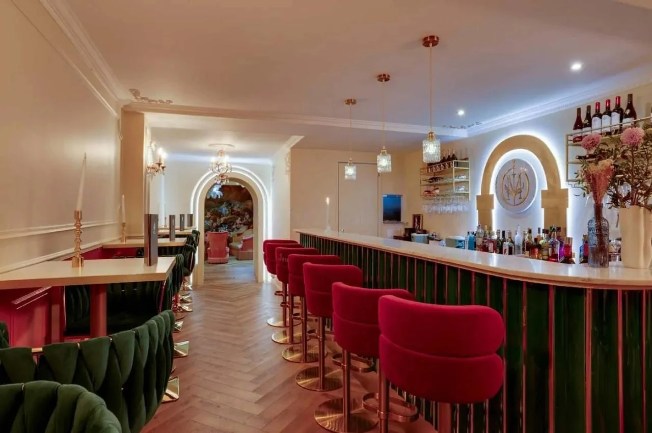 Bar with green velvet banquettes, red stools and an arched mirror