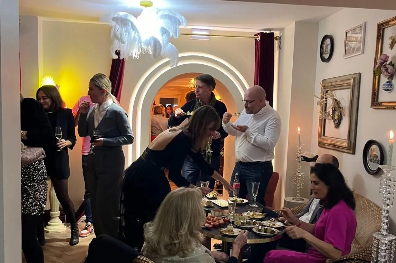 Guests at a cocktail table beneath a feather chandelier