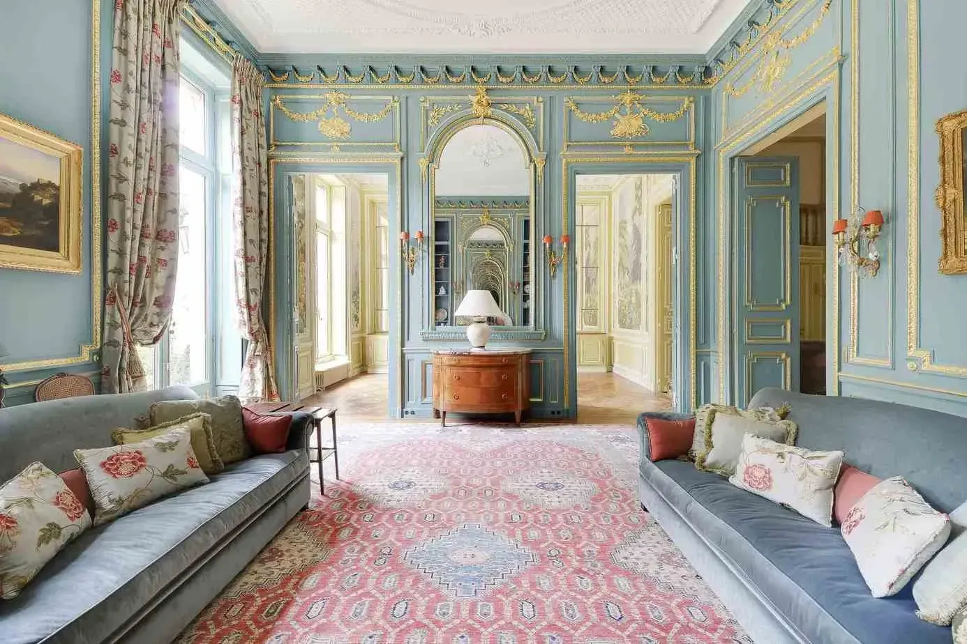 Salon with blue walls, decorative mouldings and a pink patterned rug