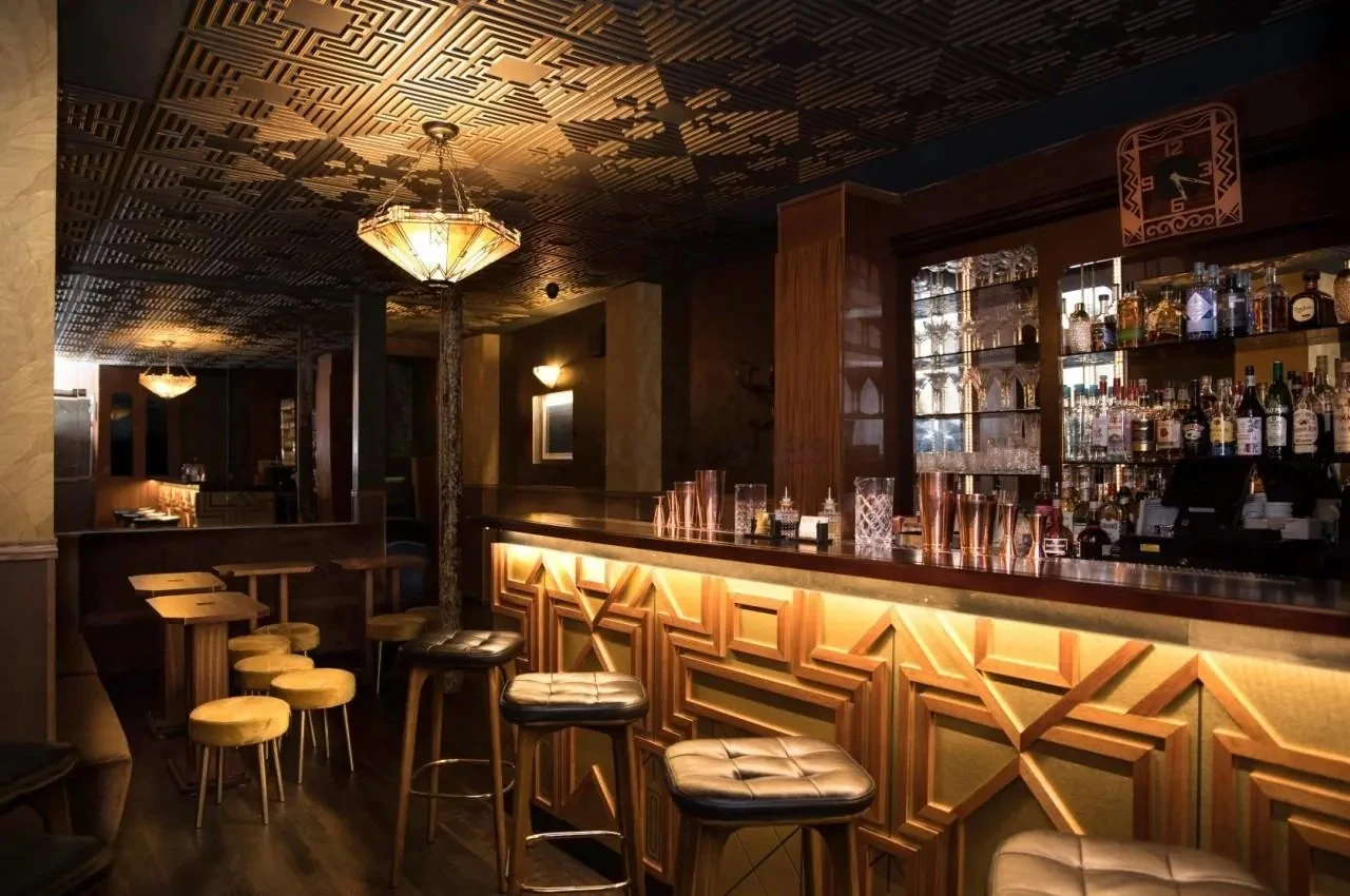 Art Deco bar with a patterned ceiling, illuminated geometric counter panels and leather stools.