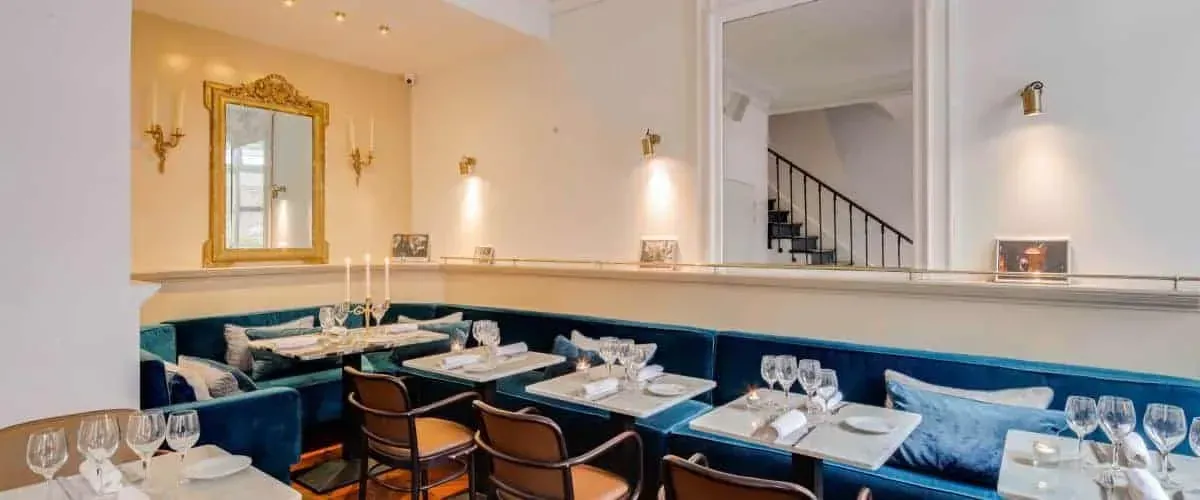 Dining room with teal banquettes and a gilded mirror above a table set for dinner