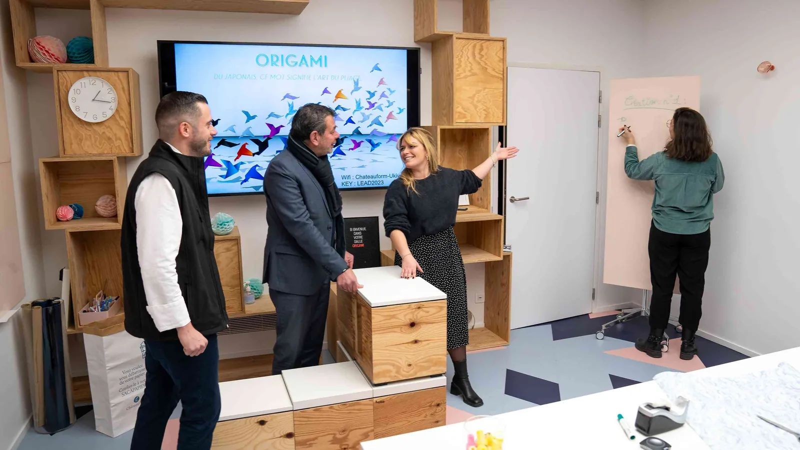 Espace de travail du Pavillon Contemporain avec écran mural, module en bois clair et personnes en réunion