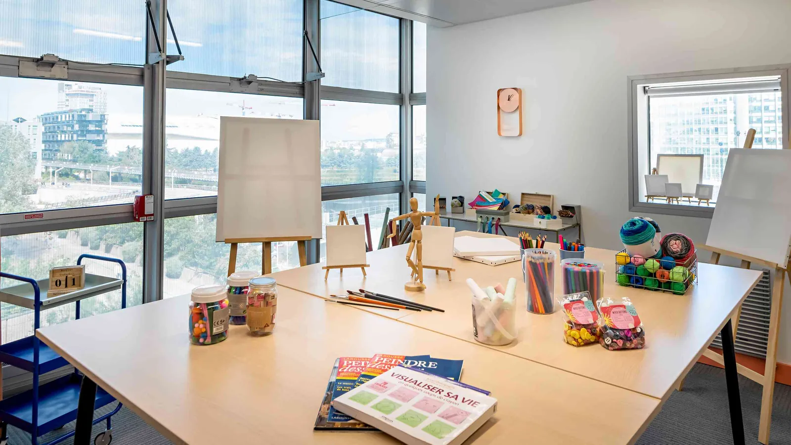 Table d'atelier créatif du Pavillon Ouest avec chevalets, peinture et grandes baies vitrées