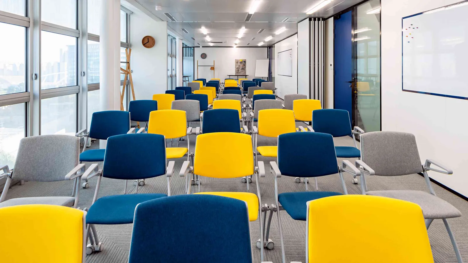Salle de formation du Pavillon Ouest avec chaises bleues et jaunes en rangs près des fenêtres