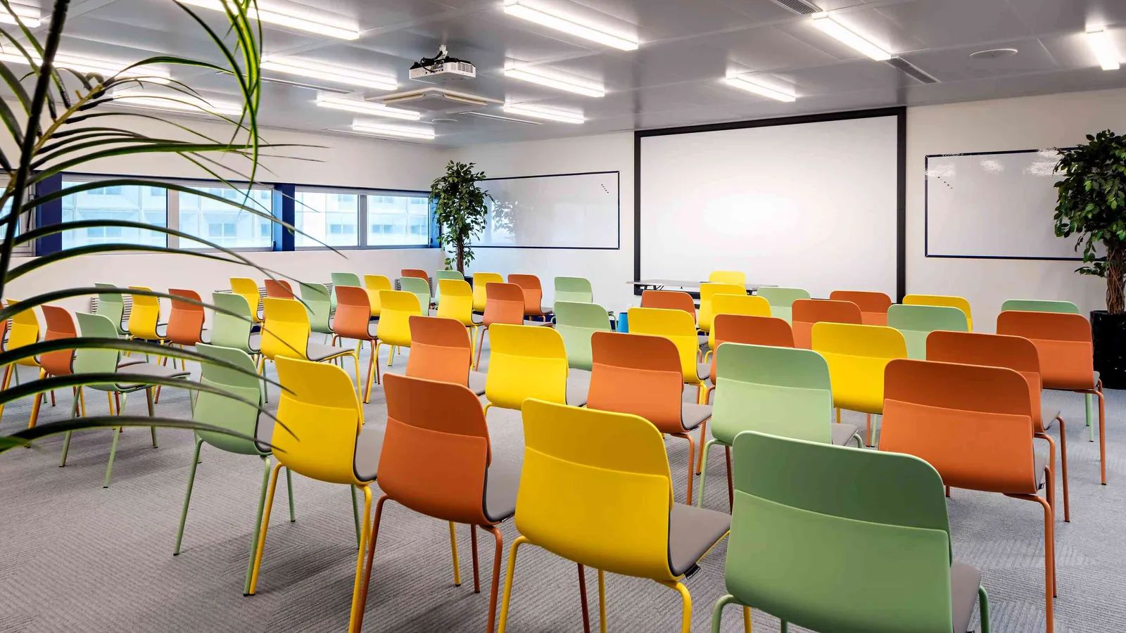 Grande salle du Pavillon Ouest avec écran de projection et rangées de chaises colorées