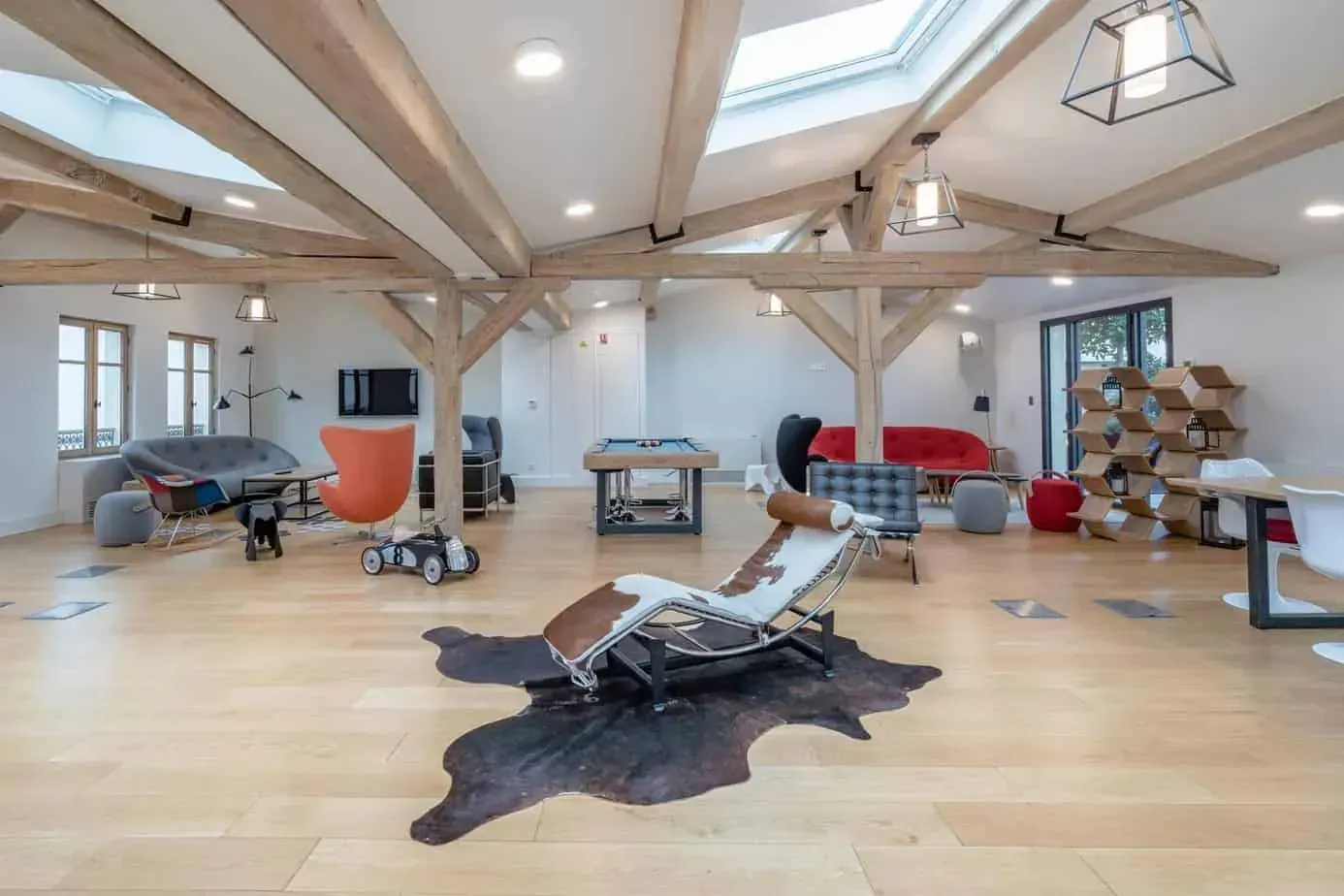 Grande pièce aux poutres apparentes, verrières et fauteuil de détente sur tapis en peau de vache