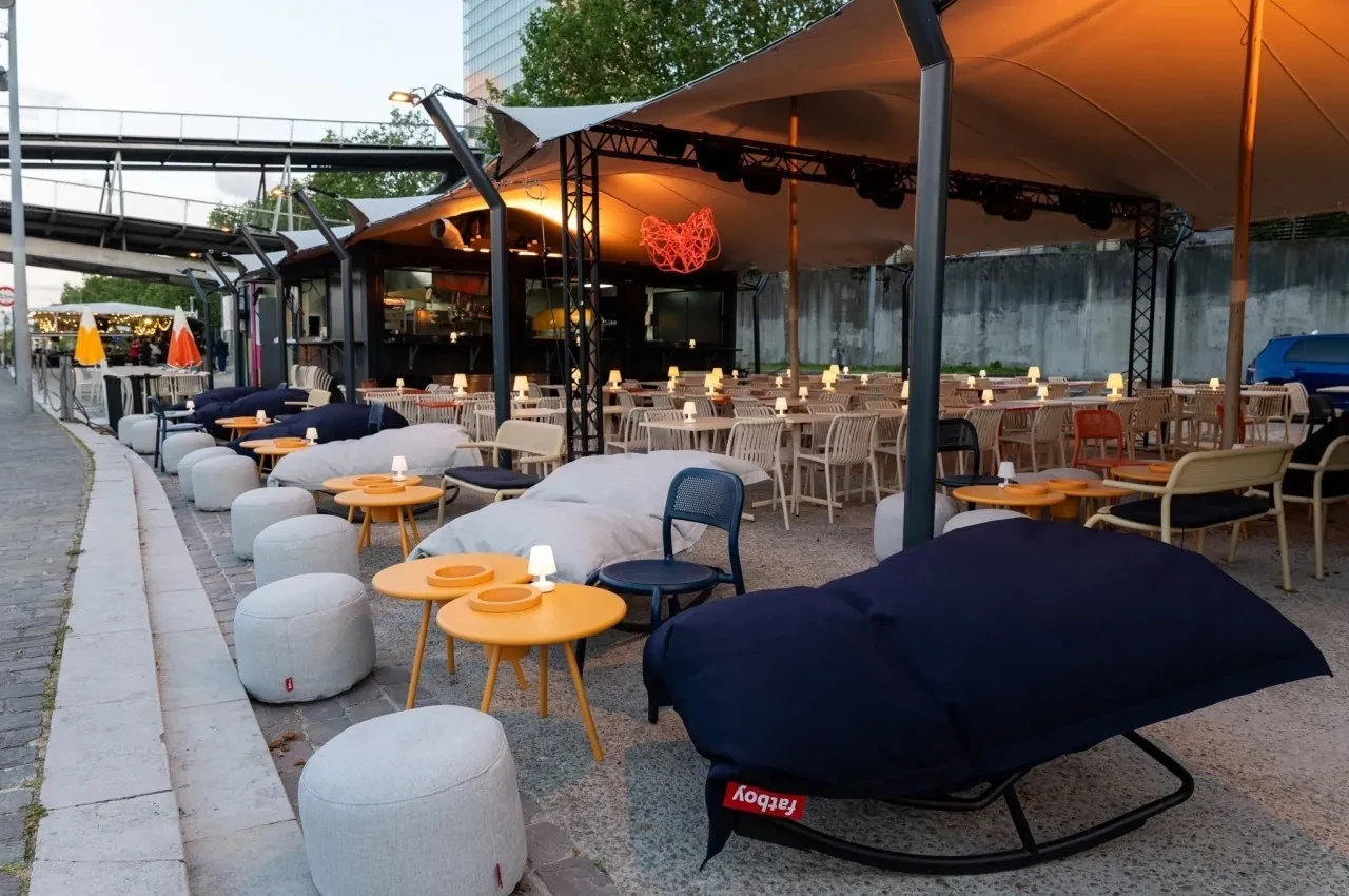 Riverside terrace with bean-bag seating, round tables and a canopy over a dining area.