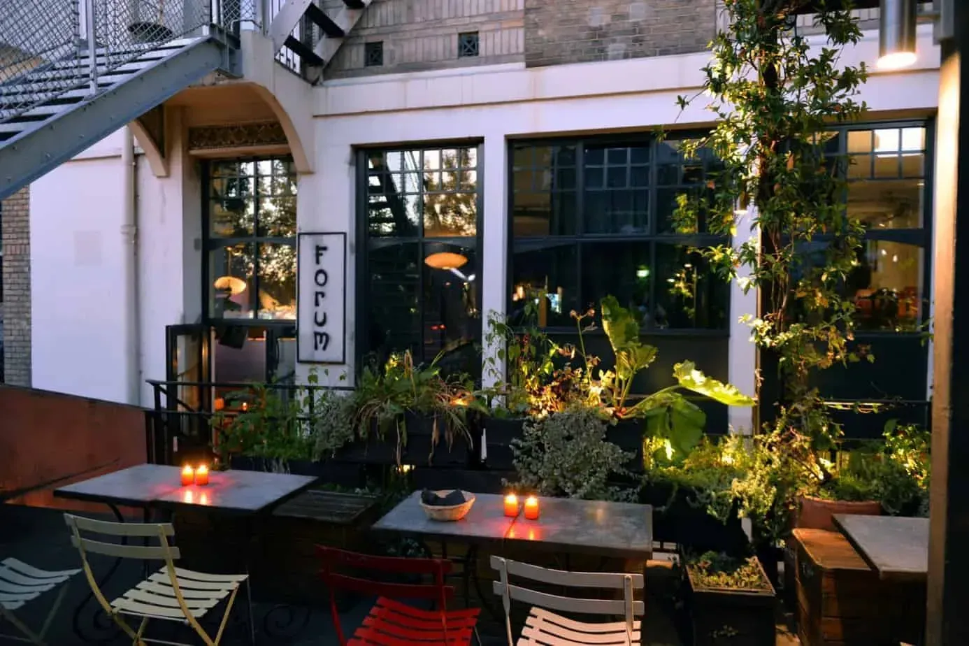 Terrasse avec plantes en pots, petites tables et chaises rouges et vertes