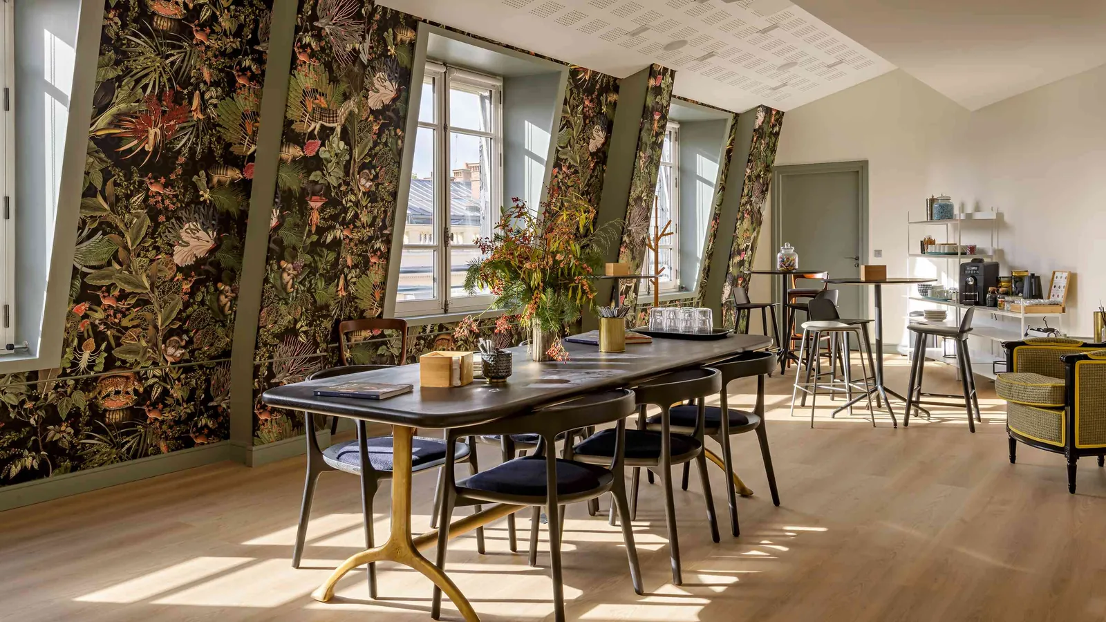 Salle des Salons des Moulures avec papier peint floral, table en bois sombre et chaises